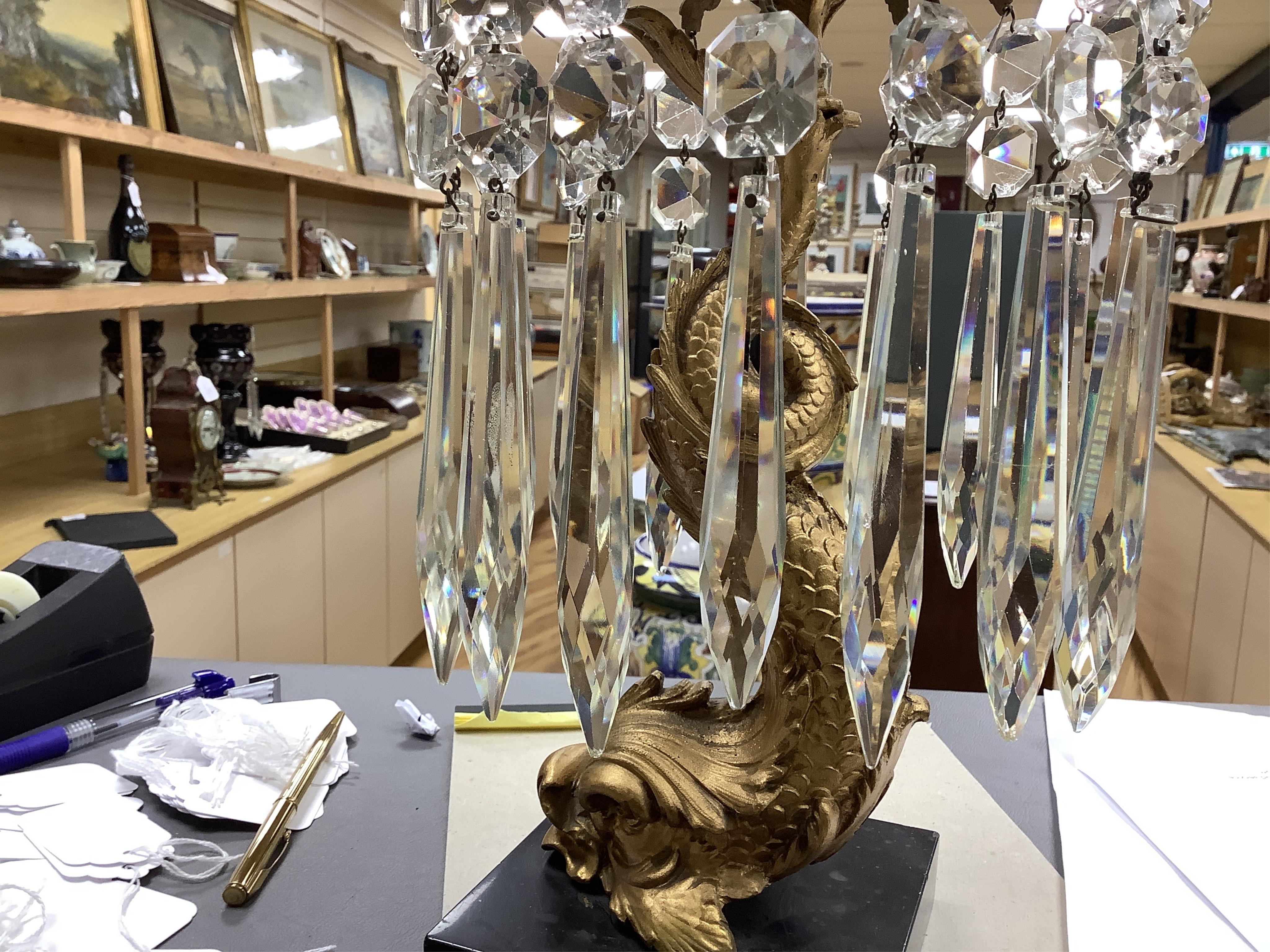 A pair of William IV gilt metal candlesticks, the stems formed as dolphins, with glass lustre drops, raised on square slate bases, 37cm high
